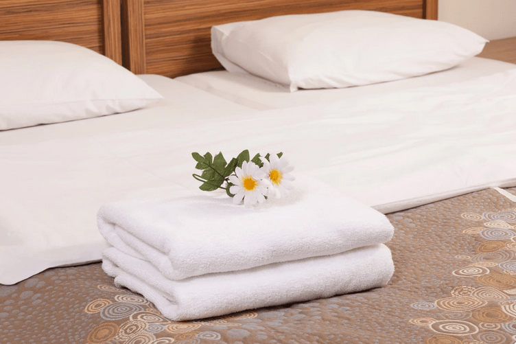schön gemachtes bett mit zwei handtüchern- darauf liegen weiße blümen