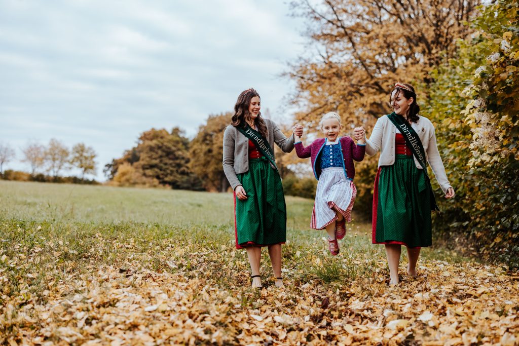 dirndlhoheiten mit kleinem mädchen im herbstlaub